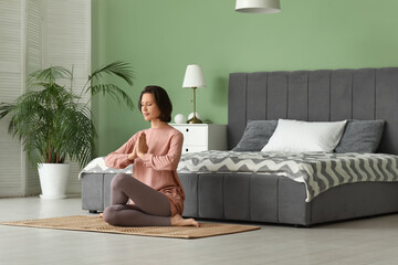 Young woman meditating while sitting on floor in bedroom