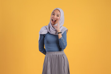 asian indonesian muslim woman shouting with cupping hand gesture on isolated yellow background