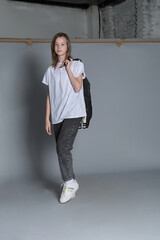 A young girl stands with a casual stance, her jacket draped over one shoulder. Dressed in jeans and...