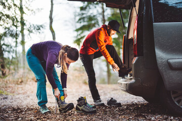 Two couple hikers preparing for a mountain hike at their camper van, after slept in it. Going on a long hike in Alps or Rocky mountains. Proper shoes and equipment is mandatory.