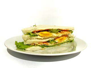 A plated of white toast bread sandwich with lettuce, sunny side up egg, hot sauce and cheese slice isolated on white background