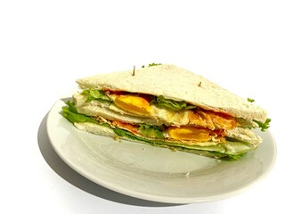 A plated of white toast bread sandwich with lettuce, sunny side up egg, hot sauce and cheese slice isolated on white background