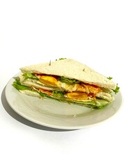 A plated of white toast bread sandwich with lettuce, sunny side up egg, hot sauce and cheese slice isolated on white background