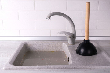 Clogged sink in the kitchen, plunger with wooden handle on the kitchen background, concept of...