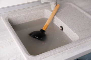 plunger with wooden handle lies in clogged sink in water, removing blockage