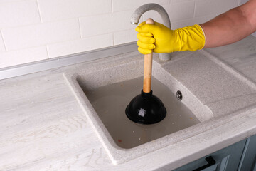 gloved hand holding plunger against clogged sink, clearing clog