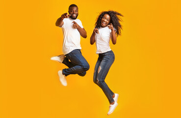 Carefree Black Millennial Man And Woman Are Jumping In The Air, yelllow background
