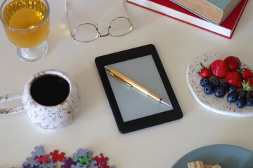 Colorful jigsaw puzzle pieces, books, tablet, glasses, cookies, berries, cup of tea or coffee, glass of juice and lit candles on the table. Hygge in pastel colors. Selective focus.