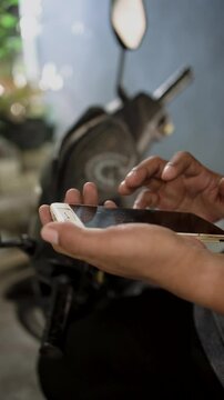 Male hand scrolls a smartphone. Close-up of man holding smartphone and scrolling through news social media feed while sitting in the motorbike.