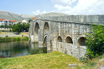 Naklejka premium Arslanagic (Perovic) Bridge - view from the Trebišnjica bank on a sunny summer day. Ottoman architectural heritage in Trebinje, Bosnia and Herzegovina: a monumental stone bridge with arches.