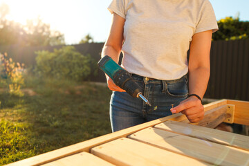 Young woman using a screwdriver while working in a workshop outdoors. Female craftsman assembles furniture