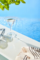 A clear glass, striped linen cloth, and sunglasses are displayed alongside a pool, leaving space for product display., creating a perfect backdrop for promoting beauty products.