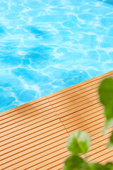 A wooden deck at the edge of a sparkling blue pool, with lush green foliage framing the scene. This image embodies and tranquility, making it perfect for promoting spa products, beauty products.