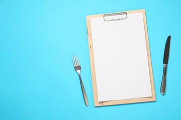Clipboard with empty paper for menu design and cutlery on light blue table, flat lay. Space for text
