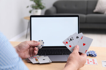Online poker. Man with playing cards, chips and laptop at wooden table indoors, closeup