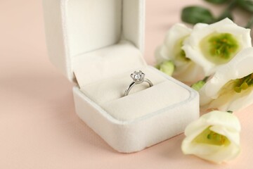 Beautiful ring with gemstone in box and flowers on pink background, closeup