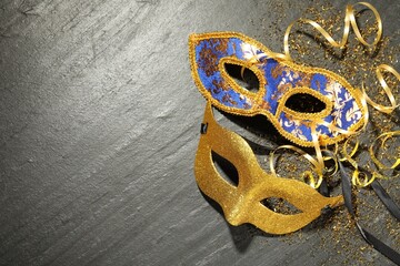 Beautiful carnival masks and confetti on gray textured table, flat lay. Space for text