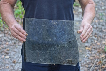 one male worker in black blue clothes holds a piece of old gray window glass in his hands on a summer street