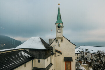 Snow-covered rooftops and a clock tower amidst the winter beauty of Salzburg draped in a soft...