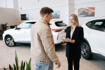 Attractive professional female car dealer in suit holding paper document, explaining buying new car...