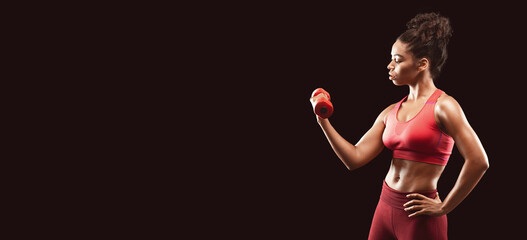 Motivated athletic afro girl working out with fitness dumbbell over black background, free space