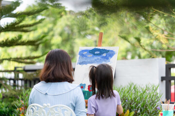 Back view mother and daughter drawing picture in garden, Woman and child girl play together in the garden