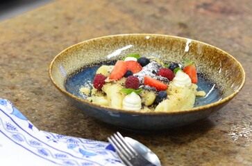 blue plate with traditional Czech sweet food, potato gnocchi with poppy seeds and cottage cheese, background of served food, fruit decorated