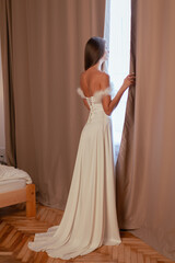 Beautiful brunette woman in white dress. Standing in the room looking out the window