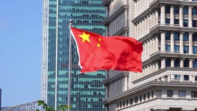 Slow motion shot of a Chinese flag waving with skyscrapers in the background. The image contrasts traditional architecture with contemporary high-rise buildings.