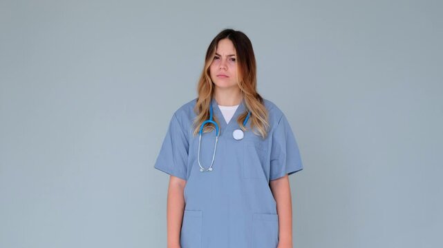 Focused Caucasian female doctor or nurse saying no and shaking head in disagreement or rejection, standing alone on gray background.
