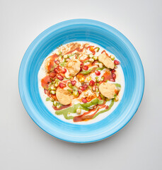 Colorful plate of chaat garnished with pomegranate seeds and green sauce served in a blue bowl