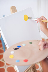 A person is painting a picture with acrylic paint and brush on a white canvas with a color palette. The scene is creative and artistic