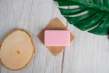 Pink soap on wooden table and and tropical monstera leaves background 