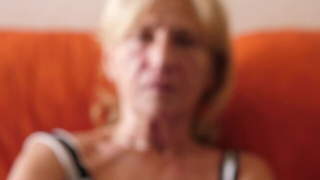 A woman sitting on the couch zapping through TV channels. Focus on the remote control and the TV screen