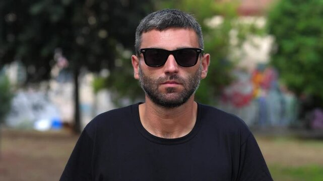 A man wearing sunglasses stares seriously into the camera, his expression stern and unyielding. The sunglasses add a touch of mystery and intensity to his gaze.