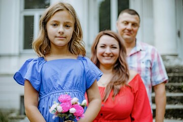 a family is posing for a picture in front of a building . the girl is holding a bouquet of flowers