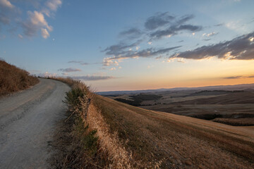 A winding dirt road on a hillside at sunset, with soft clouds and expansive rural views