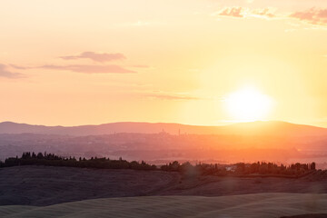 Obraz premium Orange and pink sunset over distant hills, with silhouettes of trees and a fading sky. The city of Siena as silhouette background. Sunset in Tuscany, romantic