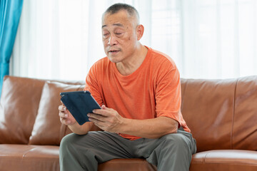 Senior man sitting on sofa and using digital tablet in living room