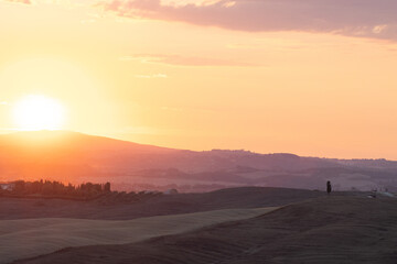 Orange and pink sunset over distant hills, with silhouettes of trees and a fading sky. The city of Siena as silhouette background. Sunset in Tuscany, romantic