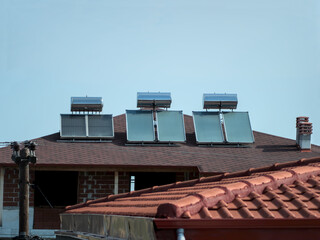 Three solar panels for water heating mounted on the top of the roof of unfinished house. Blue clear sky in the background
