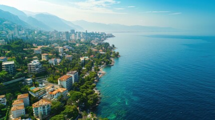 Aerial view of a coastal city with a mix of residential buildings,&nbsp;green spaces,&nbsp;and a vast blue sea under a clear sky
