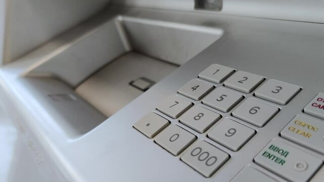 Female hand entering pin code on ATM keypad and putting money in money slot