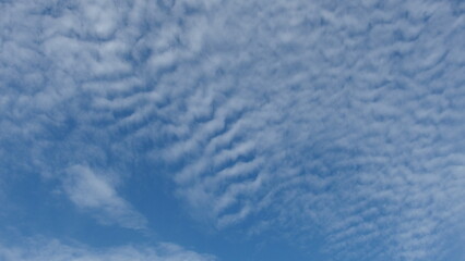 a sky filled with a pattern of clouds known as altocumulus clouds. These clouds appear as white or gray patches, often with a wavy or rippled texture. The sky is mostly covered with these clouds