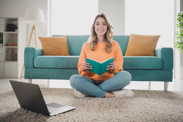 Full length photo of nice cheerful girl sit floor netbook read book dressed orange garment spend pastime spacious house indoors room