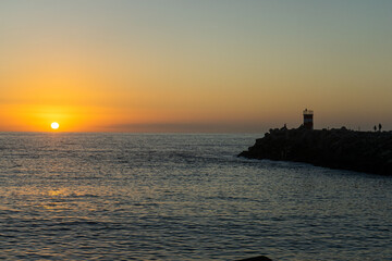 A breathtaking sunset at Nazaré, Portugal, with the sun dipping below the horizon, framed...