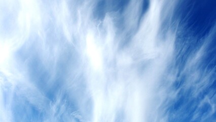 a section of the sky with wispy, white clouds against a bright blue background. The clouds appear to be thin and stretched out, resembling cirrus clouds, which are typically high-altitude clouds
