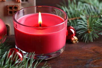 Burning candle, Christmas decor and fir tree branches on wooden table, closeup