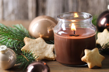 Burning candle, baubles, cookies and fir branches on wooden table, closeup. Christmas atmosphere