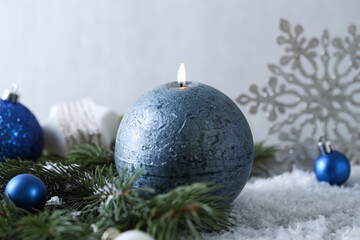 Burning candle, baubles and fir branches on artificial snow, closeup. Christmas atmosphere